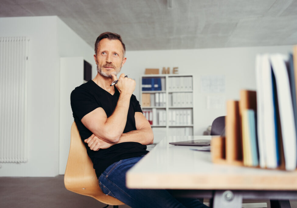 thoughtful man sitting at his desk in front of a laptop in his home office