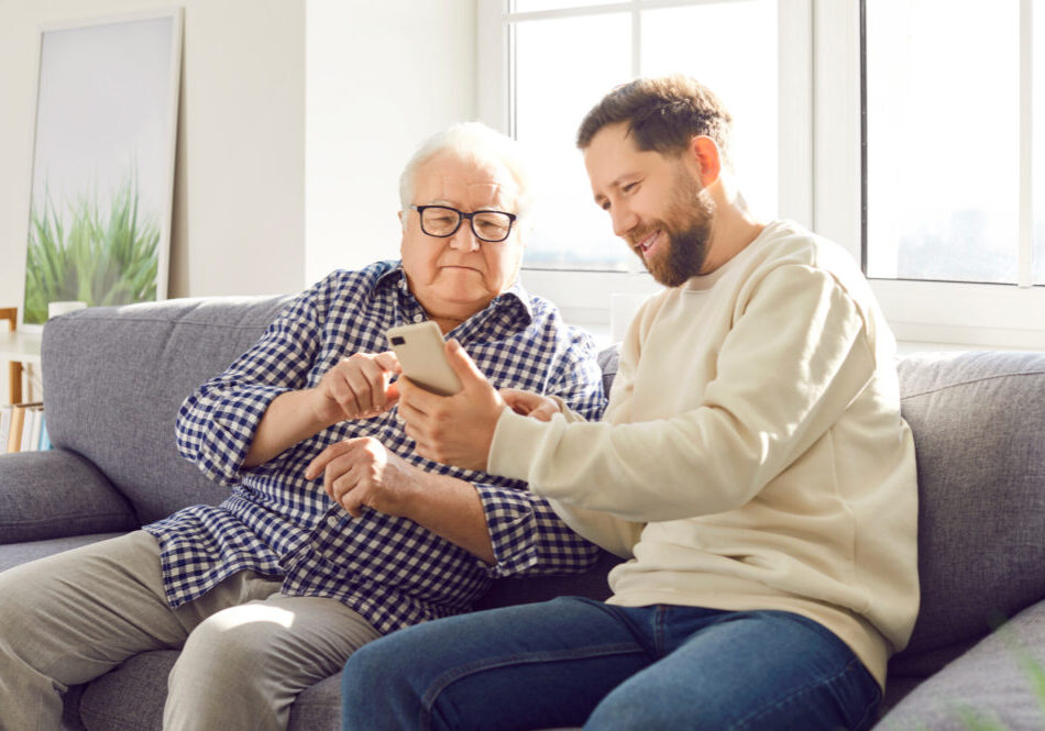 Son Helps Elderly Father With Phone And Modern Technology.